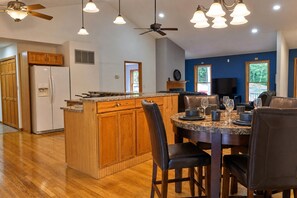 Une cuisine moderne avec des meubles en bois, un plan de travail en granit et un coin repas doté de chaises en cuir et d’une table en marbre.