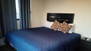 A bedroom with a bed, a headboard, a nightstand, and a window with curtains.