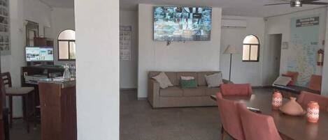 Una sala de estar con sofá, televisor montado en la pared, mesa de comedor con sillas y ventilador de techo.