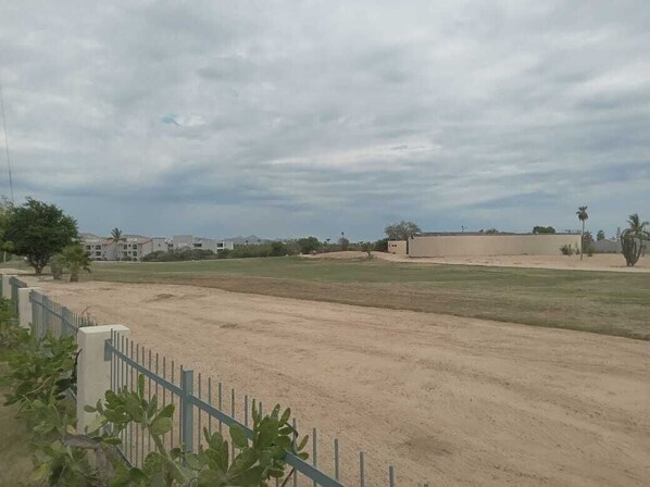 A large open field with a fence, buildings in the background, and a cloudy sky.
