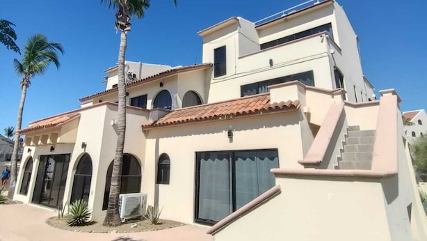 A multi-story building with a pool, palm trees, and a clear blue sky.