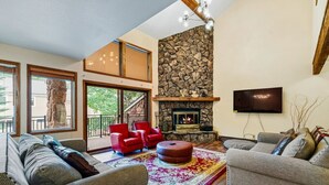 A spacious living room with a stone fireplace, red chairs, and a large window overlooking a balcony. - Spacious Keystone Family Escape Great Location (Keystone)