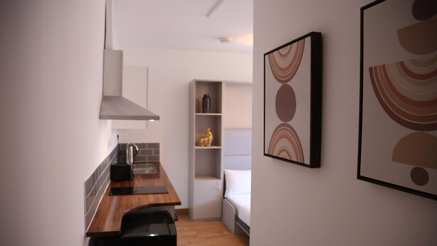 A compact kitchen with a wooden countertop, a built-in stove, and a white cabinet. There is a small shelf with decorative items and a framed abstract painting on the wall. - Stylish Studio Escape (London)