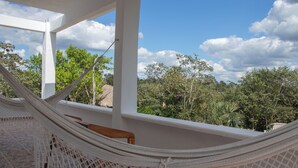A hammock on a balcony with a view of a lush garden and a clear sky.