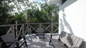 An outdoor deck with wooden furniture, including two chairs and a table, surrounded by a wooden railing and trees.