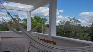 A hammock on a stone-tiled patio with a view of trees and a clear sky.