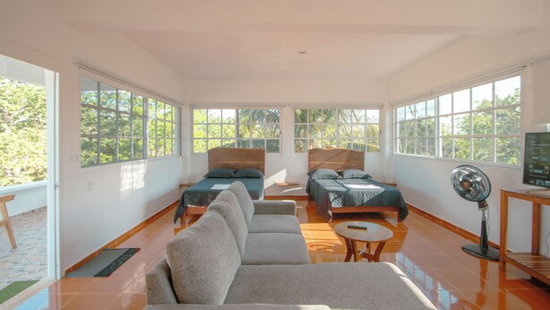 A spacious room with two beds, a sofa, a fan, and large windows.