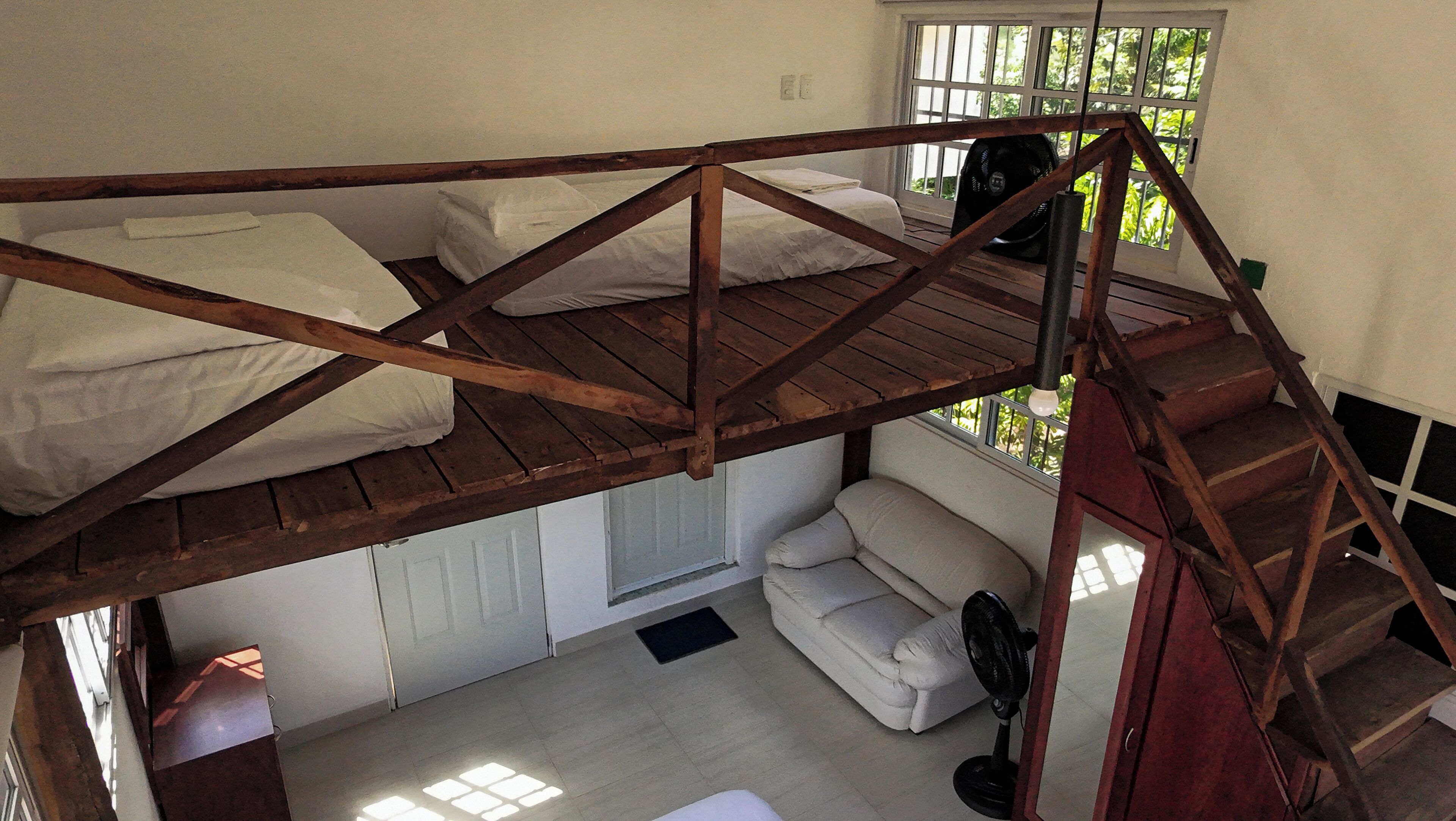 A loft-style bedroom with a wooden bunk bed, a sofa, and a staircase.