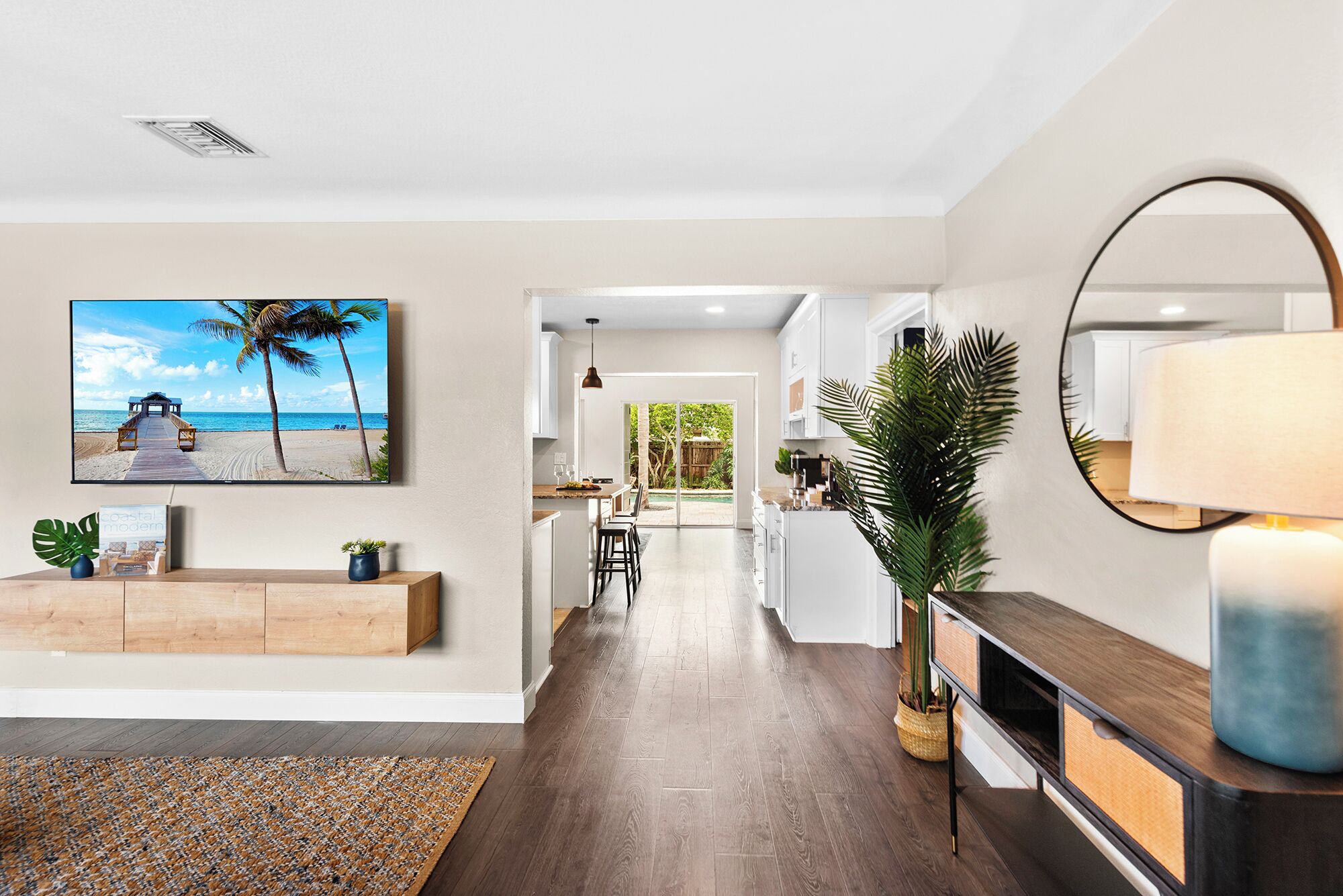 A modern kitchen with white cabinets, a wooden countertop, and a large island. There is a dining area with a table and chairs, and a view of the backyard through a glass door.