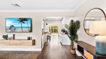A modern kitchen with white cabinets, a wooden countertop, and a large island. There is a dining area with a table and chairs, and a view of the backyard through a glass door.