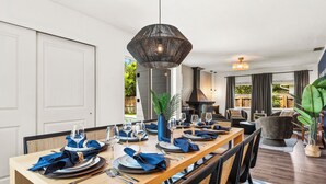 Un comedor con una larga mesa de madera dispuesta para seis comensales, rodeada de sillas con respaldo trenzado. Una lámpara colgante grande se encuentra sobre la mesa.