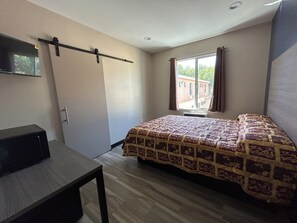 Ein Schlafzimmer mit Bett, Schreibtisch, Fenster mit Vorhängen und Blick auf Gebäude.