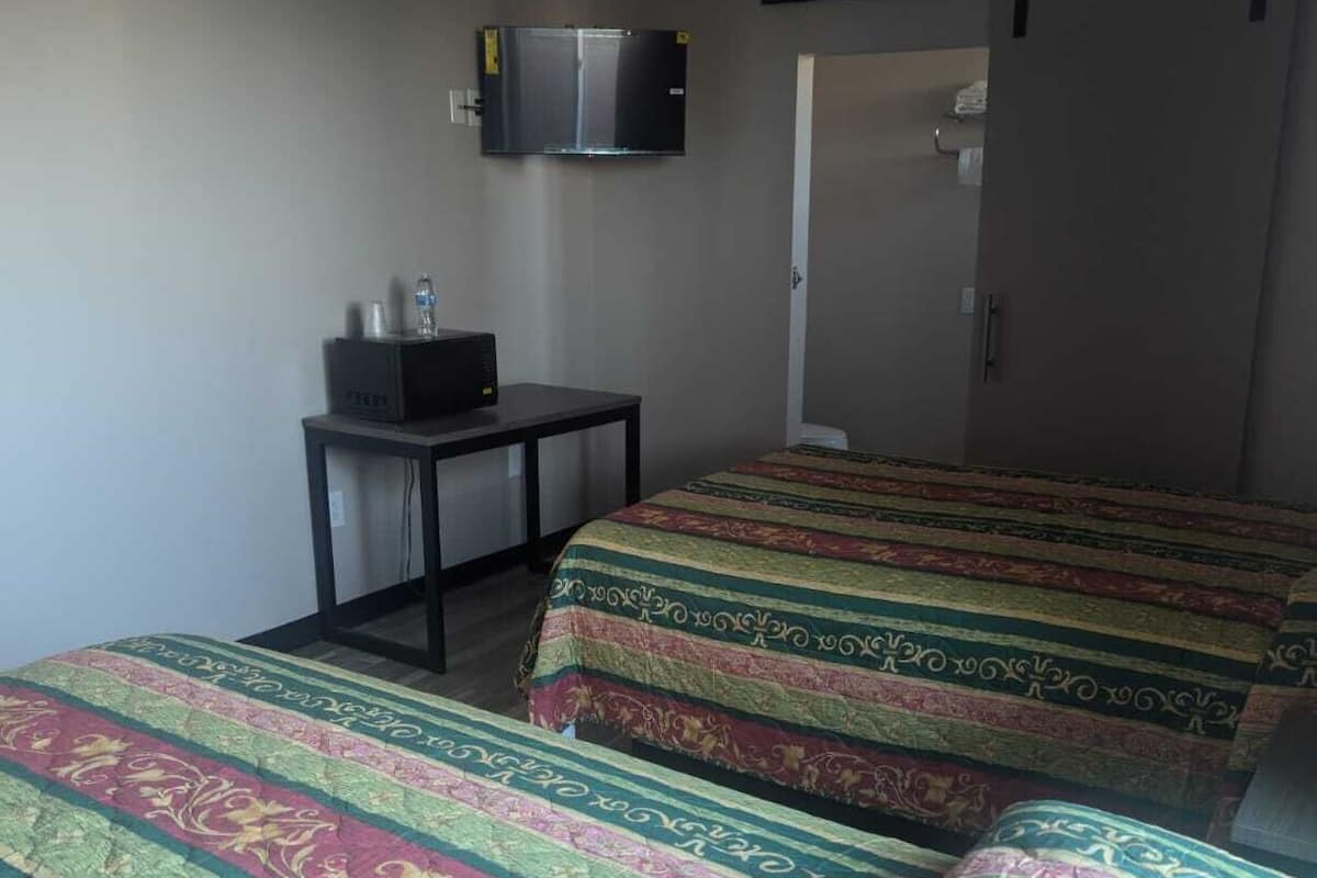 A hotel room with two beds, a television mounted on the wall, and a small table with a water bottle and glasses.