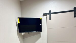 Ett rum med en platt-TV som är monterad på väggen, en mikrovågsugn på ett träbord och en skjutdörr.