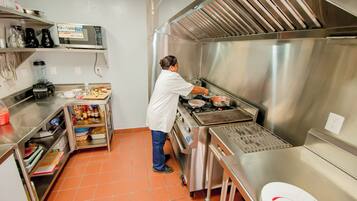 A commercial kitchen with stainless steel appliances, a person cooking, and various kitchen tools and ingredients.
