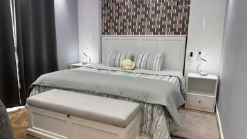 A modern bedroom with a bed, bedside tables, a bench, and a patterned wall.