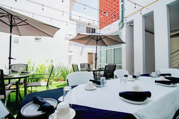 An outdoor dining area with tables set for two, umbrellas, and chairs.