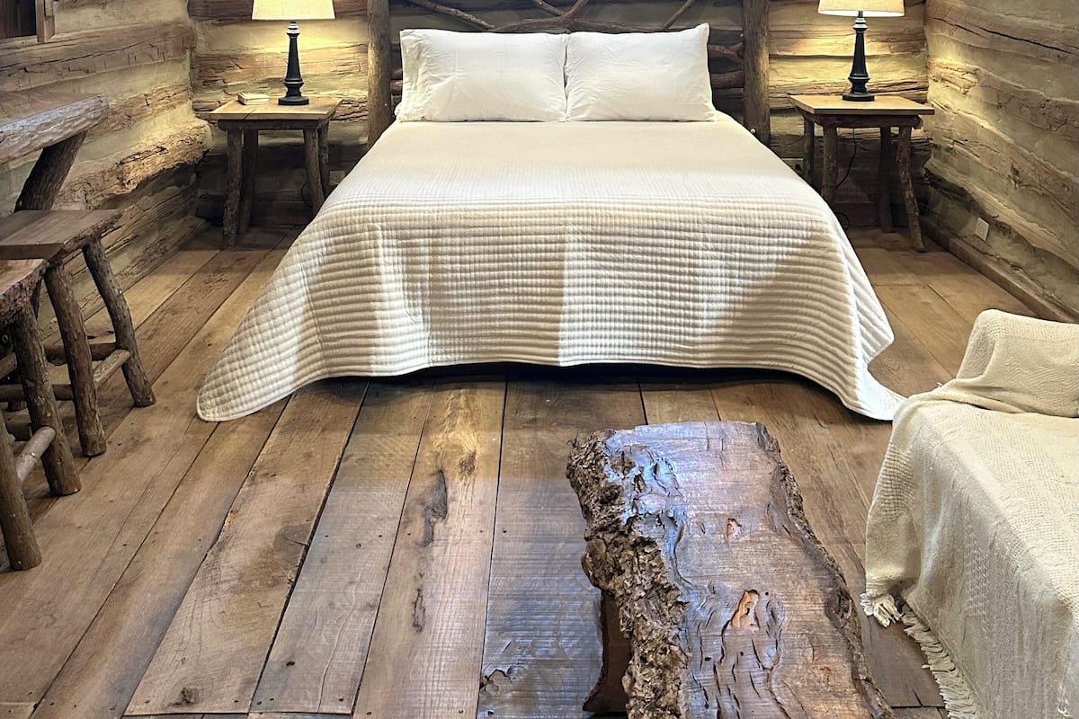 Ein Schlafzimmer in einer Blockhütte mit einem großen Bett, zwei Nachttischlampen und einem rustikalen Holz-Kopfteil.