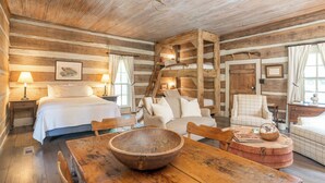 L’intérieur d’un chalet rustique, avec un lit en bois, une table à manger surmontée d’un grand saladier et une échelle menant à une mezzanine.