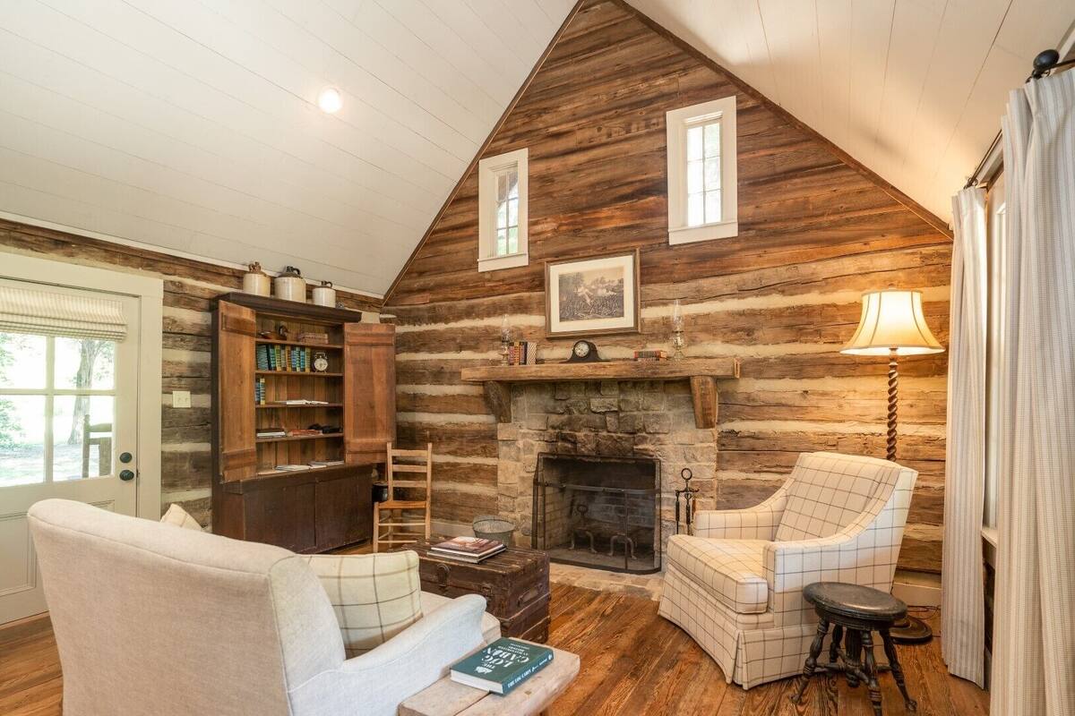 Ein gemütliches Blockhaus-Interieur mit Kamin, einer Bücherwand, einer komfortablen Sitzecke und einer Wendeltreppe zu einem Erkerraum.