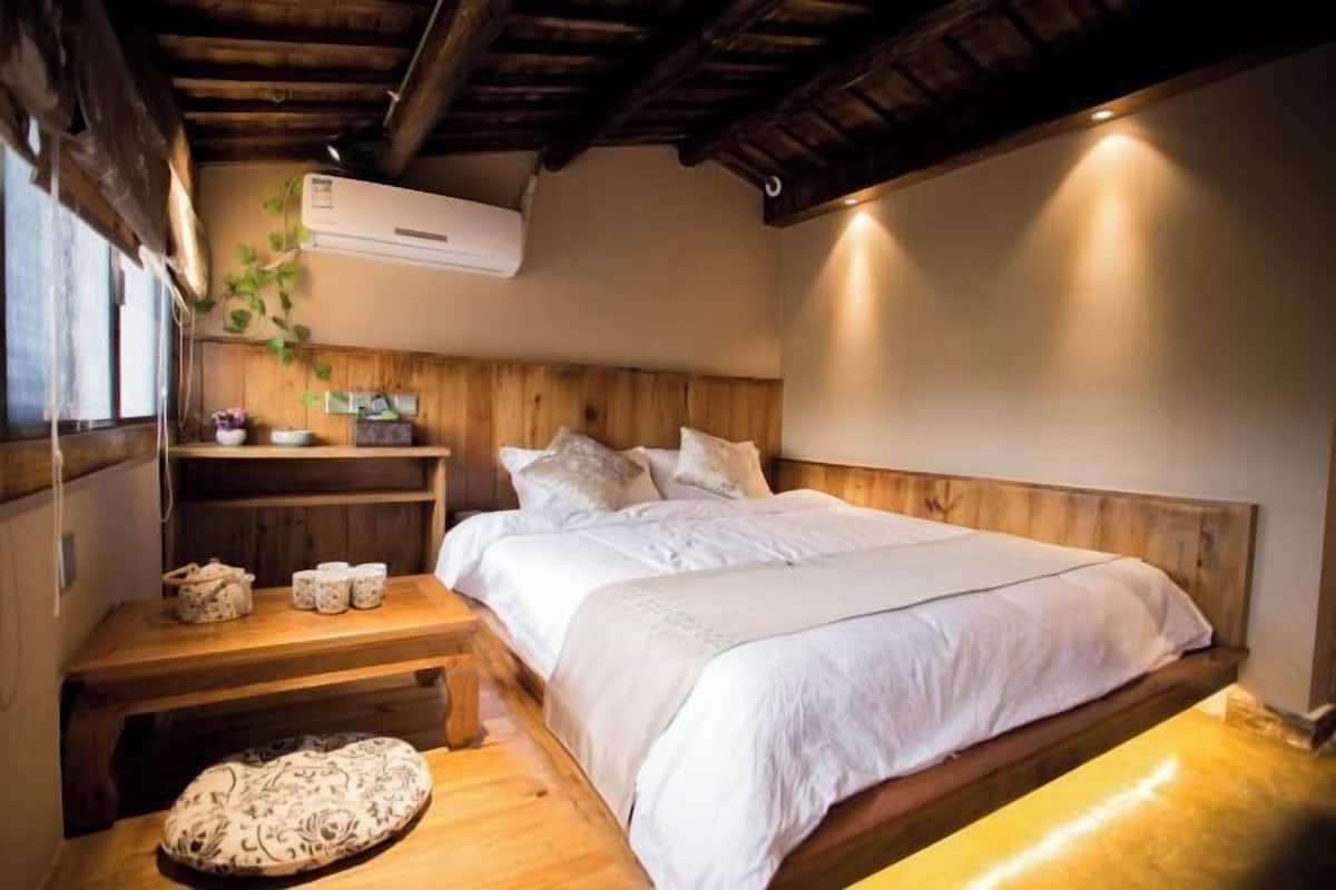 A cozy bedroom with a wooden headboard, a bedside table with a lamp, and a small plant.