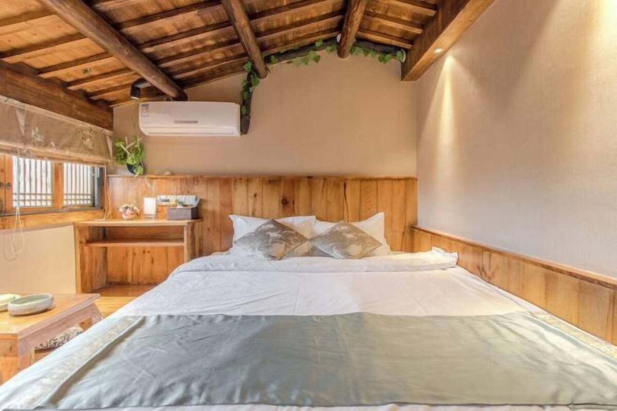 A wooden-framed room with a bed, a small desk, and a window with blinds.