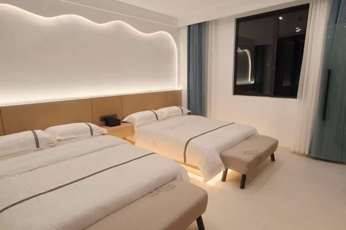 A hotel room with two beds, a nightstand, a bench, a large window, and a modern headboard.