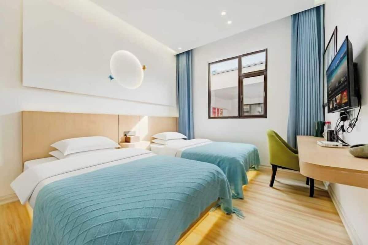 A hotel room with two beds, a desk, a chair, a TV, and a window with curtains.