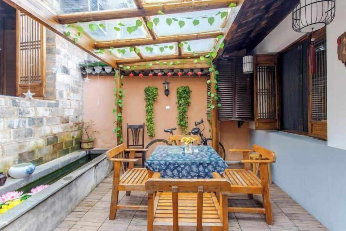 A courtyard with a wooden table and chairs, a small water feature, and a pergola with climbing plants.