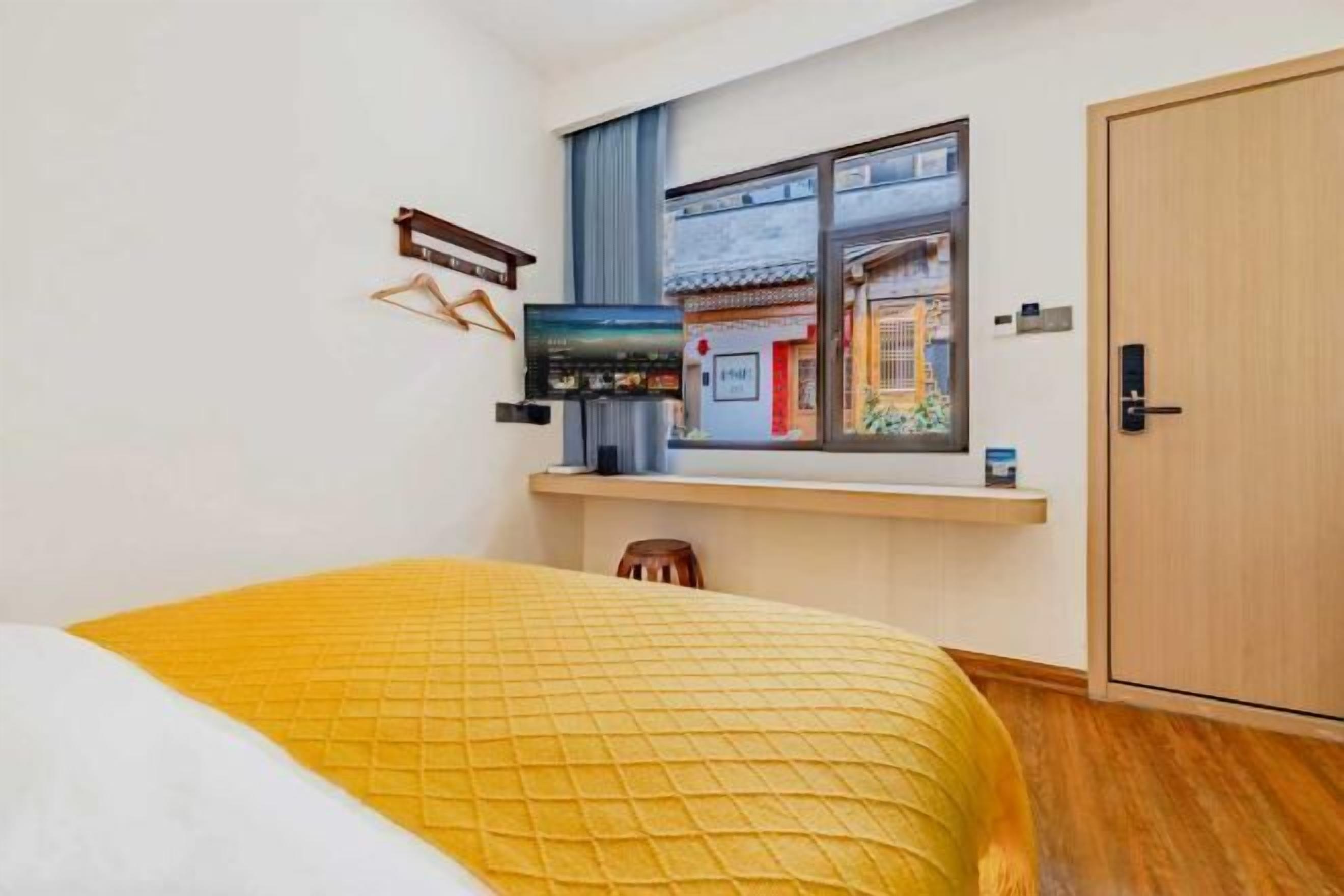 Ein Zimmer mit einem Bett, einem Fernseher auf einem Regal, einem Kleiderschrank und einem Fenster mit Blick auf ein Gebäude.