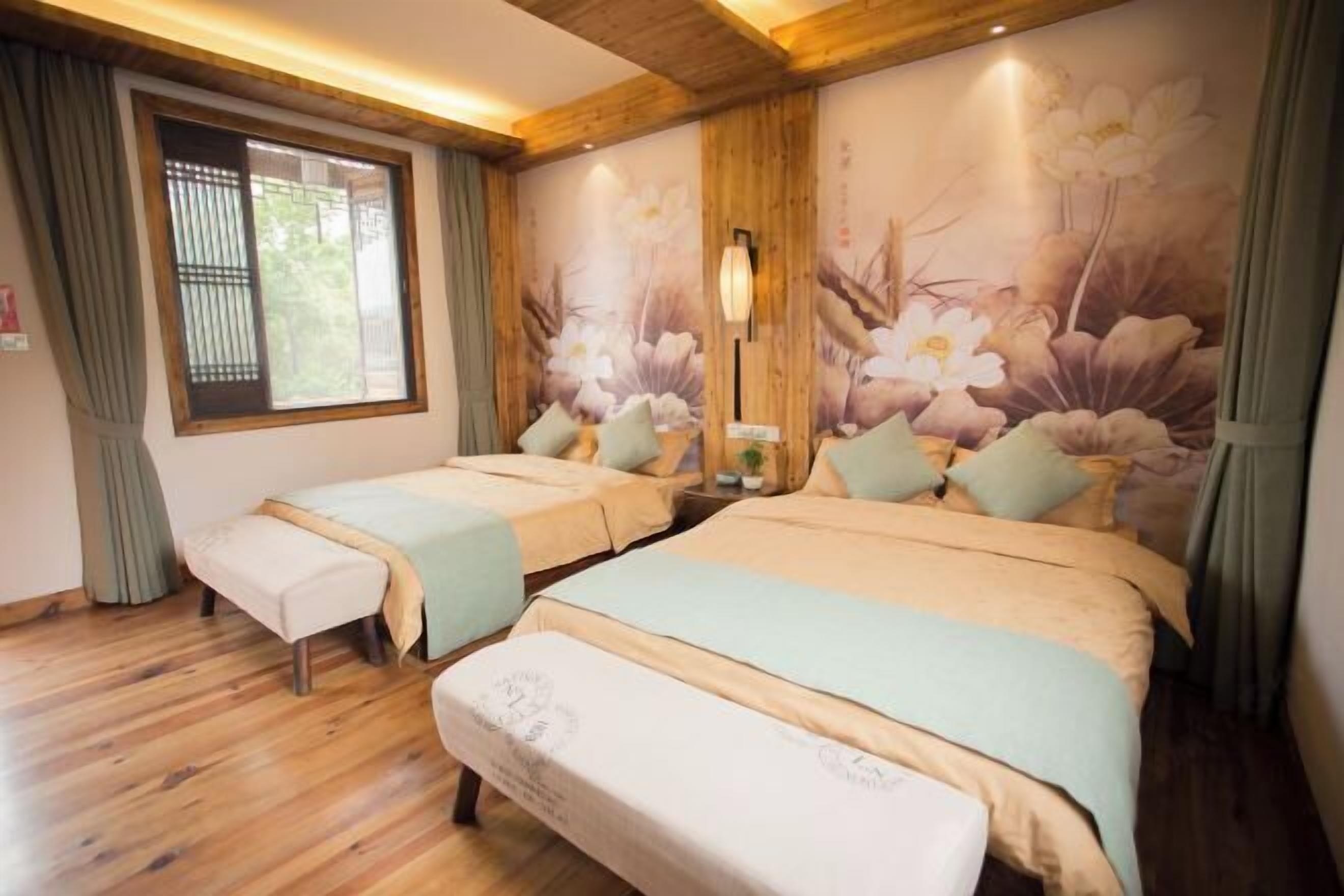 A hotel room with two beds, wooden flooring, a window with curtains, and a floral wall mural.