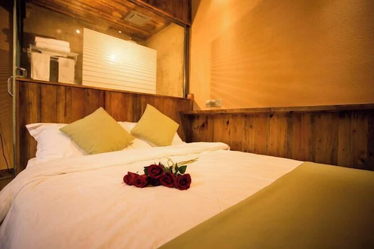 A neatly made bed with a bouquet of red roses, wooden walls, and a window with blinds.