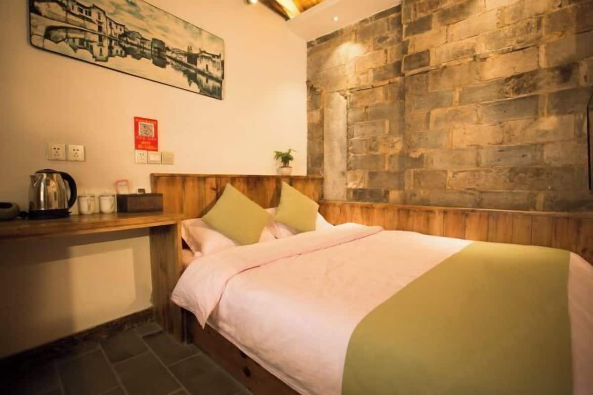A cozy bedroom with a stone wall, a wooden headboard, and a bed with a pink and green bedspread.