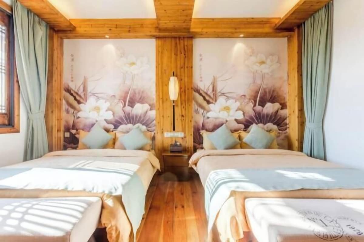 A room with two beds, wooden ceiling beams, floral wall art, and a nightstand between the beds.