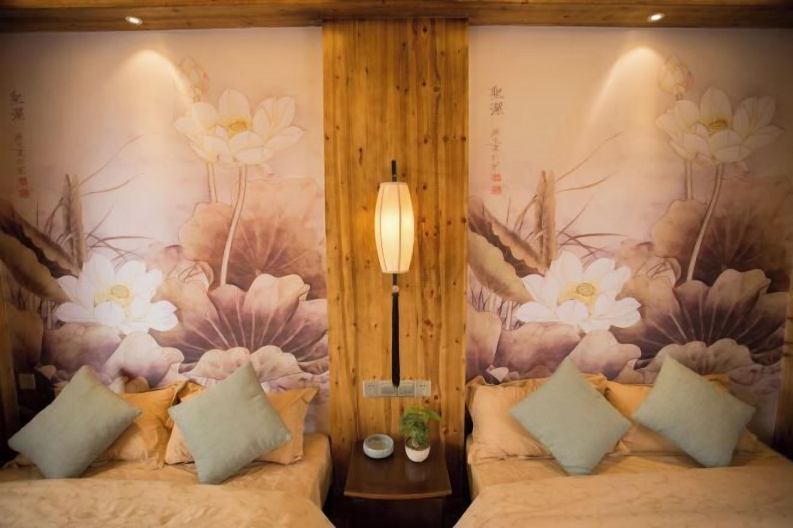 A room with a wooden ceiling, a central light fixture, and a wall mural of flowers. There are two sofas with cushions and a small table with a plant.