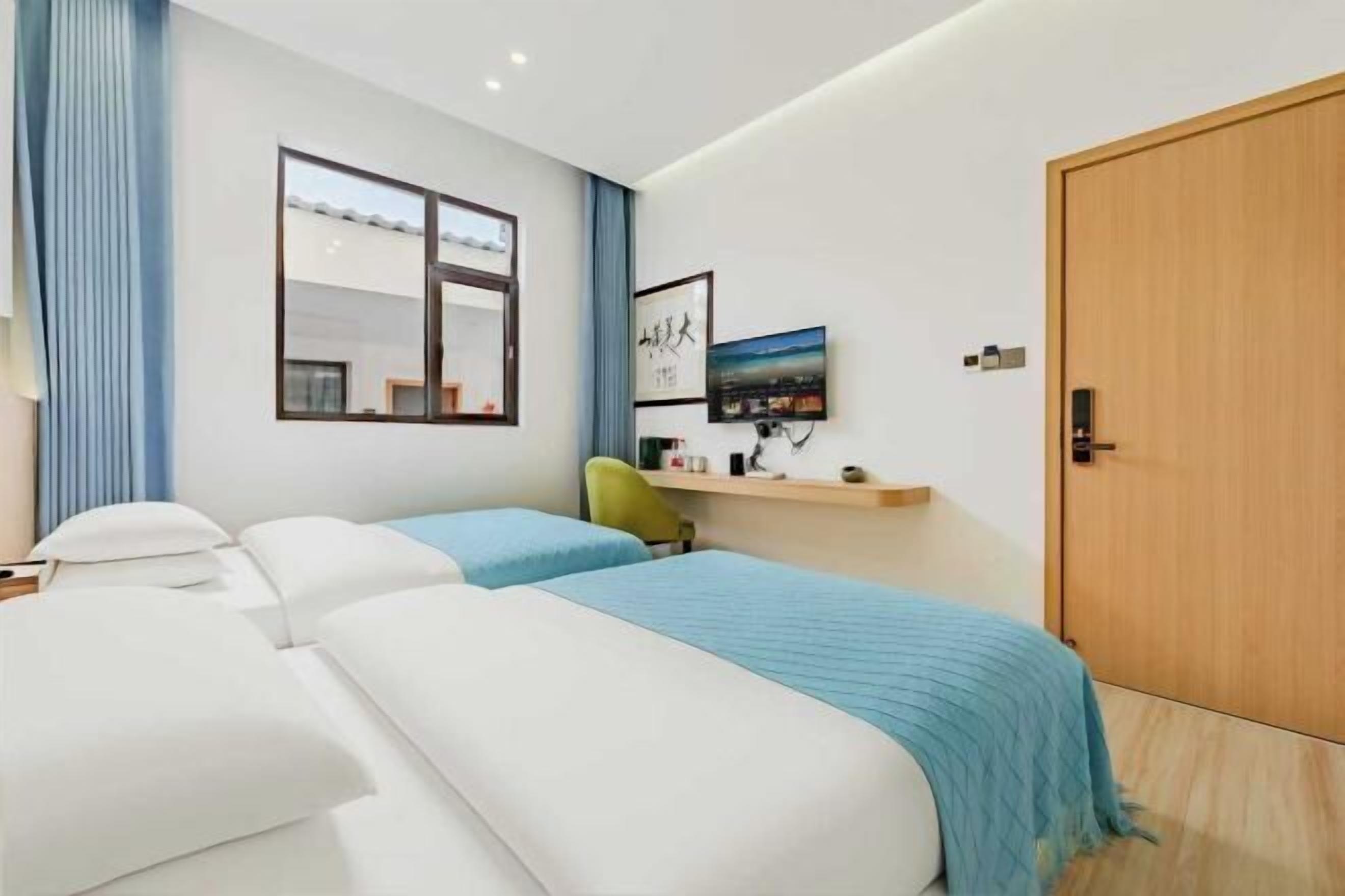 Een moderne hotelkamer met twee bedden, een bureau, een stoel, een televisie en een houten deur.