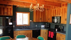 A kitchen with wooden cabinets, a black refrigerator, a stove, and a dining table with chairs.