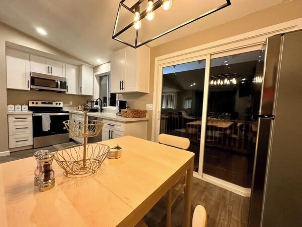 A modern kitchen with white cabinets, stainless steel appliances, and a wooden dining table.