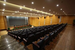 Un teatro con file di sedili neri, un palco con uno schermo e un muro in legno con un motivo decorativo.