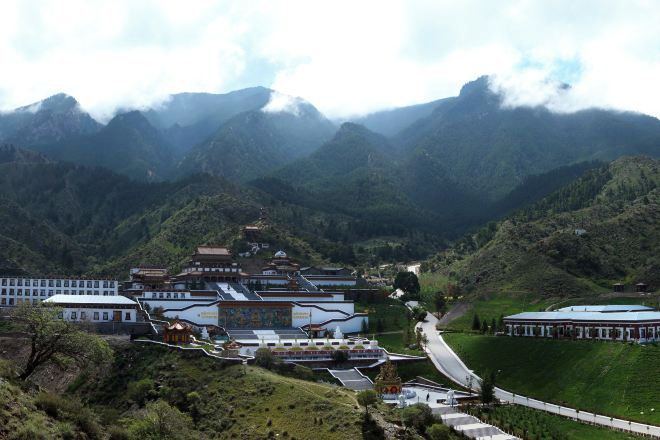 A traditional building complex with multiple structures, surrounded by lush green hills and mountains.
