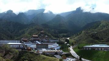 A traditional building complex with multiple structures, surrounded by lush green hills and mountains.