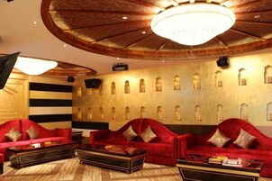 Un lobby de hotel con una imponente lámpara de araña, sofás rojos y una pared con estampado.