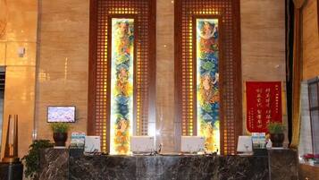 A reception area with a marble counter, two vertical screens with colorful artwork, a television, and a red banner on the wall.