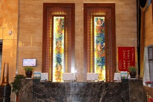 Una zona de recepción con mostrador de mármol, dos pantallas verticales con obras de arte coloridas, un televisor y un cartel rojo en la pared.