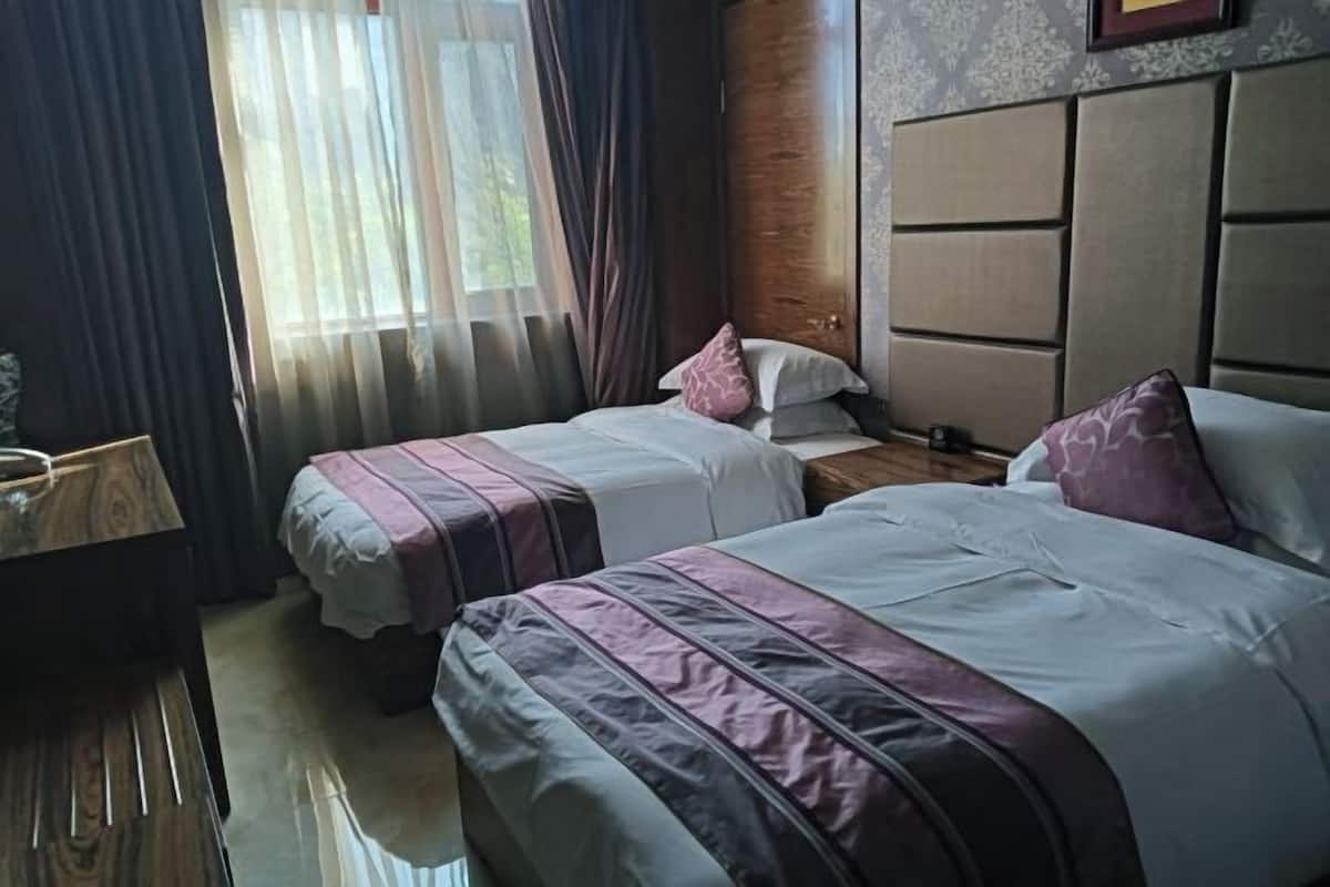 A hotel room with two beds, a wooden desk, and a window with curtains.