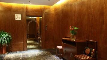 A lobby with wooden paneling, a reception desk, a chair, and a potted plant.