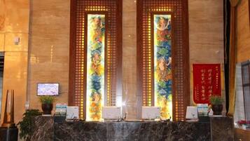 A reception area with a marble counter, two vertical stained glass panels, a television screen, and a red sign with Chinese characters.