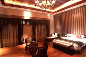 A hotel room with a large bed, a desk, a chair, and a sofa. - Helan Mountain Forest Park Visitor Service Center (Alxa Left Banner)