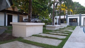 Un espace extérieur moderne avec un chemin en béton, des palmiers et une voiture garée.