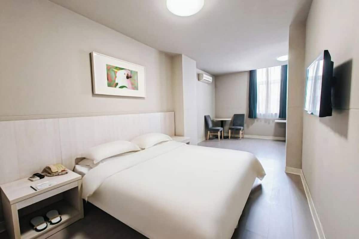 Una habitación de hotel con cama, mesita de noche, silla, televisor y una obra de arte en la pared.